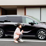 **

A sleek, modern Honda Odyssey minivan parked in front of a stylish urban home in Japan. The lighting is soft and warm, highlighting the car's refined design. Focus on the front grille and sharp headlights. Include a family of four (parents and two young children) happily getting into the car, suggesting a weekend trip. The overall impression should be one of sophistication and comfort.

**